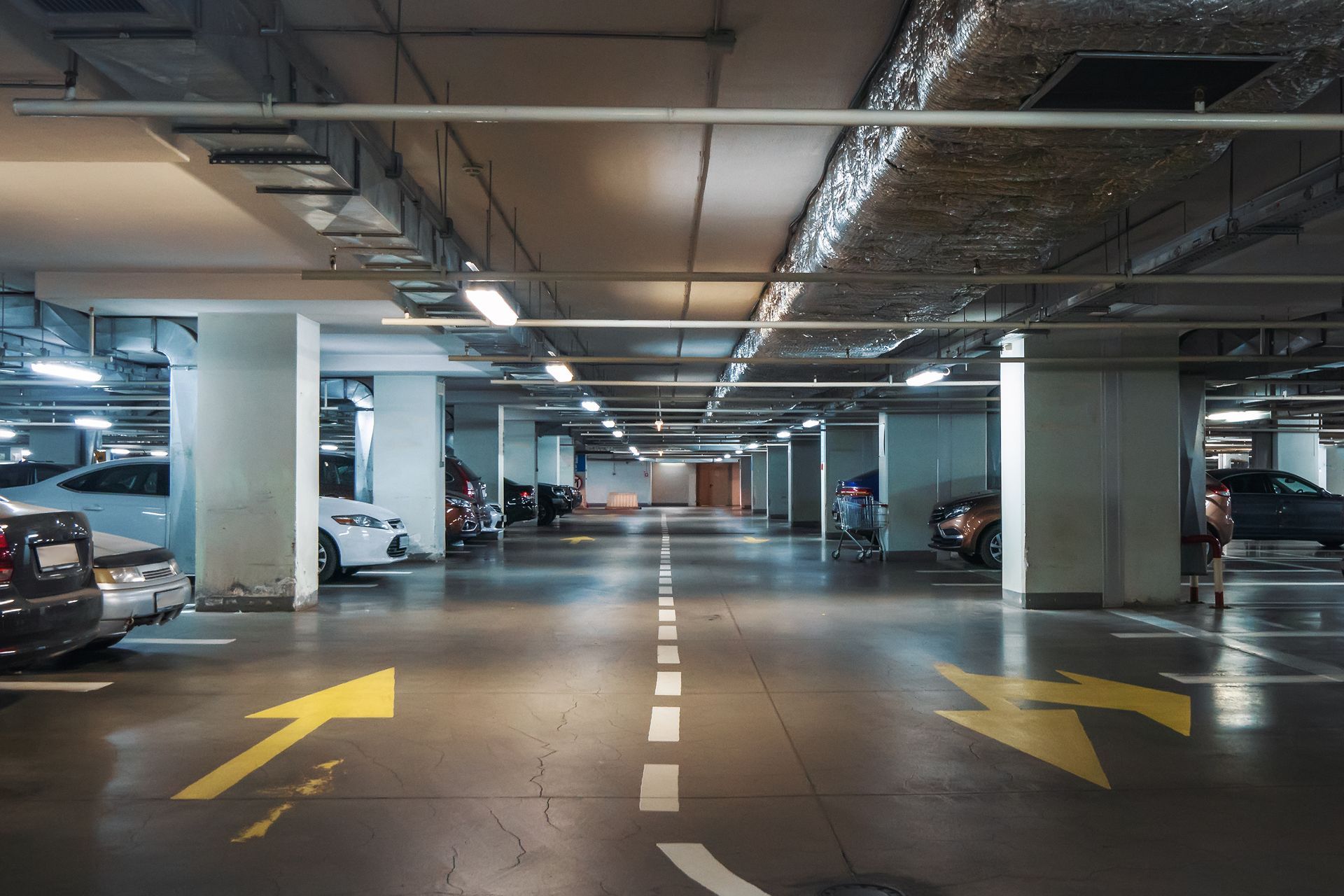 Underground parking garage with marked lanes, yellow arrows, parked cars, and concrete columns