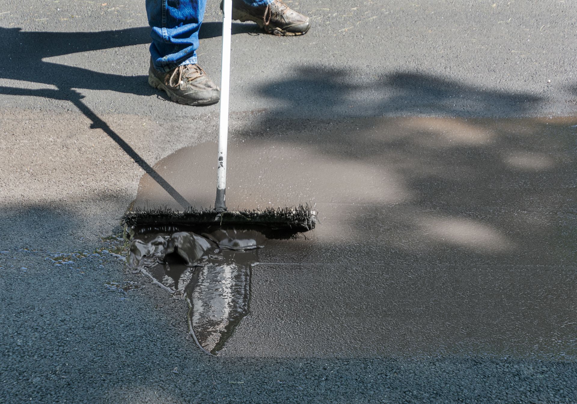 Person using a white squeegee to spread black asphalt sealant on pavement Person using a white squeegee to spread black asphalt sealant on pavement