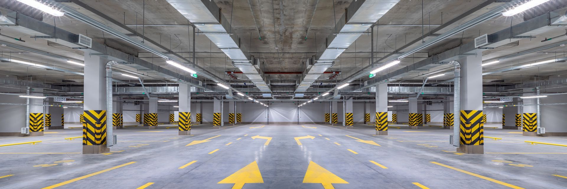 Empty underground parking garage with yellow directional arrows and black-yellow striped columns Empty underground parking garage with yellow directional arrows and black-yellow striped columns