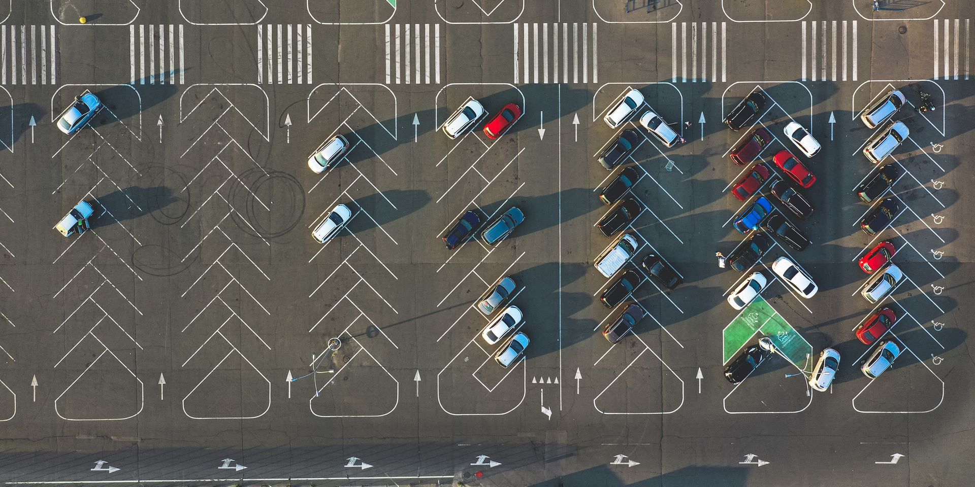 Aerial view of a parking lot with several parked cars, mostly empty spaces, and painted diagonal parking lines. Aerial view of a parking lot with several parked cars, mostly empty spaces, and painted diagonal parking lines.