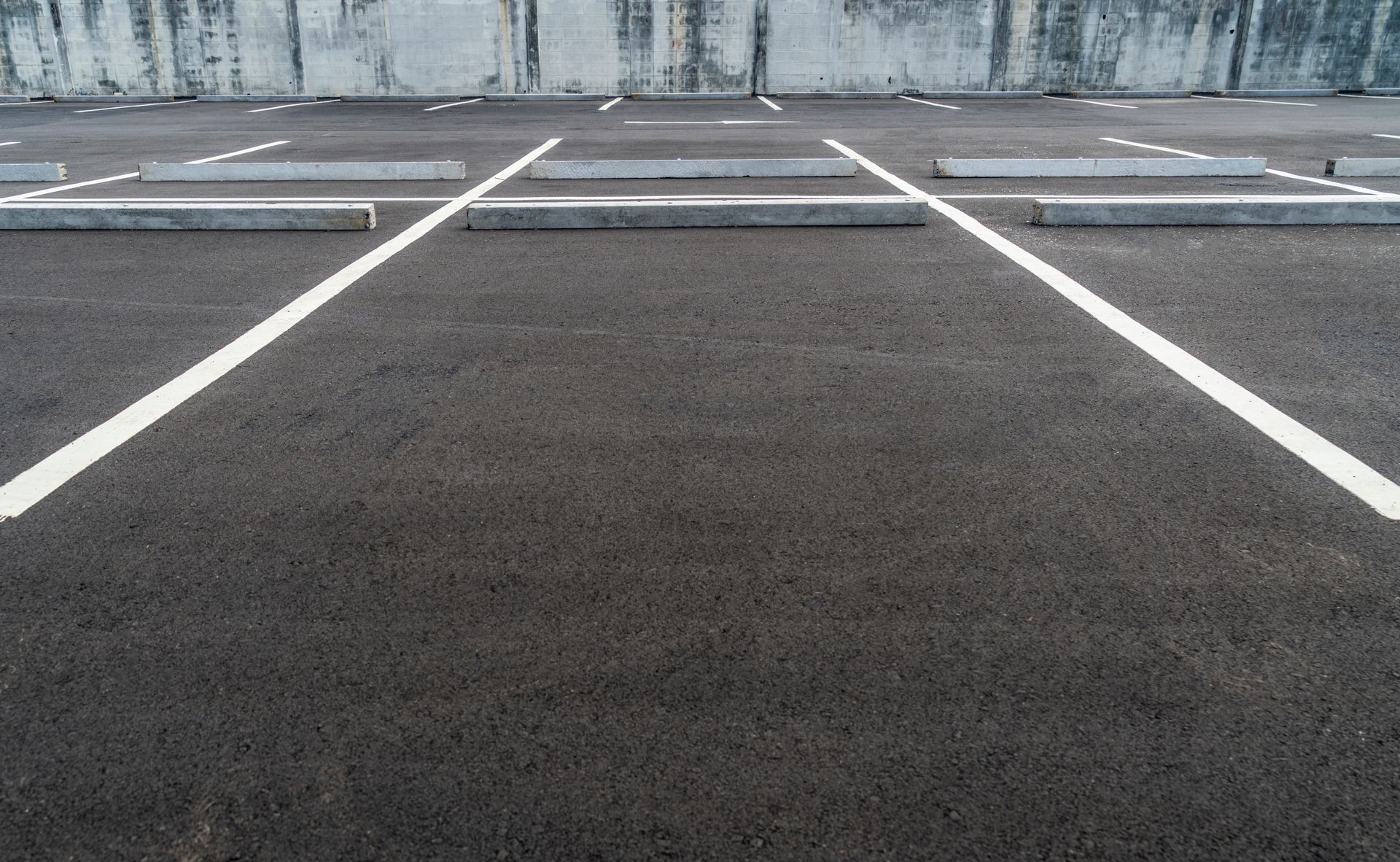 Empty parking lot with white painted lines in front of a concrete wall Empty parking lot with white painted lines in front of a concrete wall