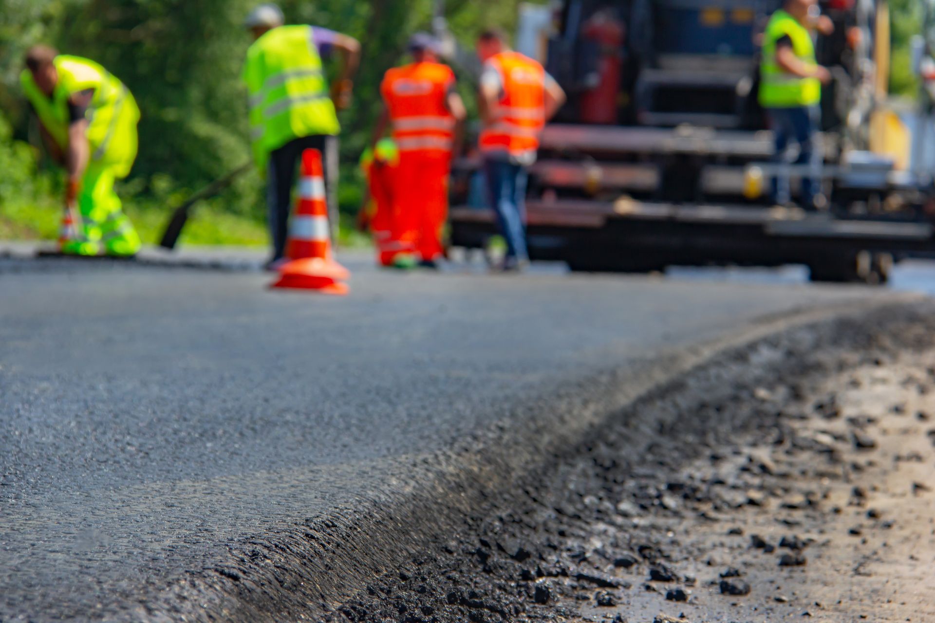 Road workers in high-visibility gear paving a street beside traffic cones.