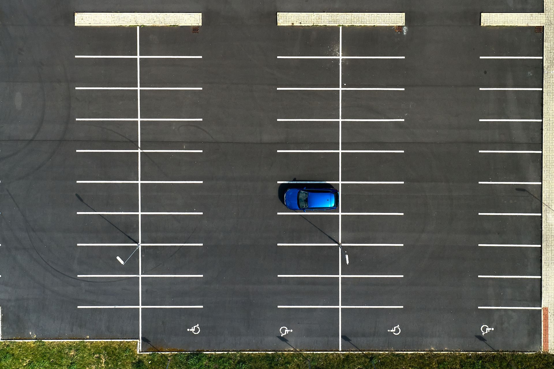Blue car in a mostly empty parking lot, seen from above. Blue car in a mostly empty parking lot, seen from above.