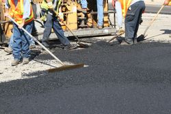 Road crew paving asphalt with rakes around a construction vehicle
