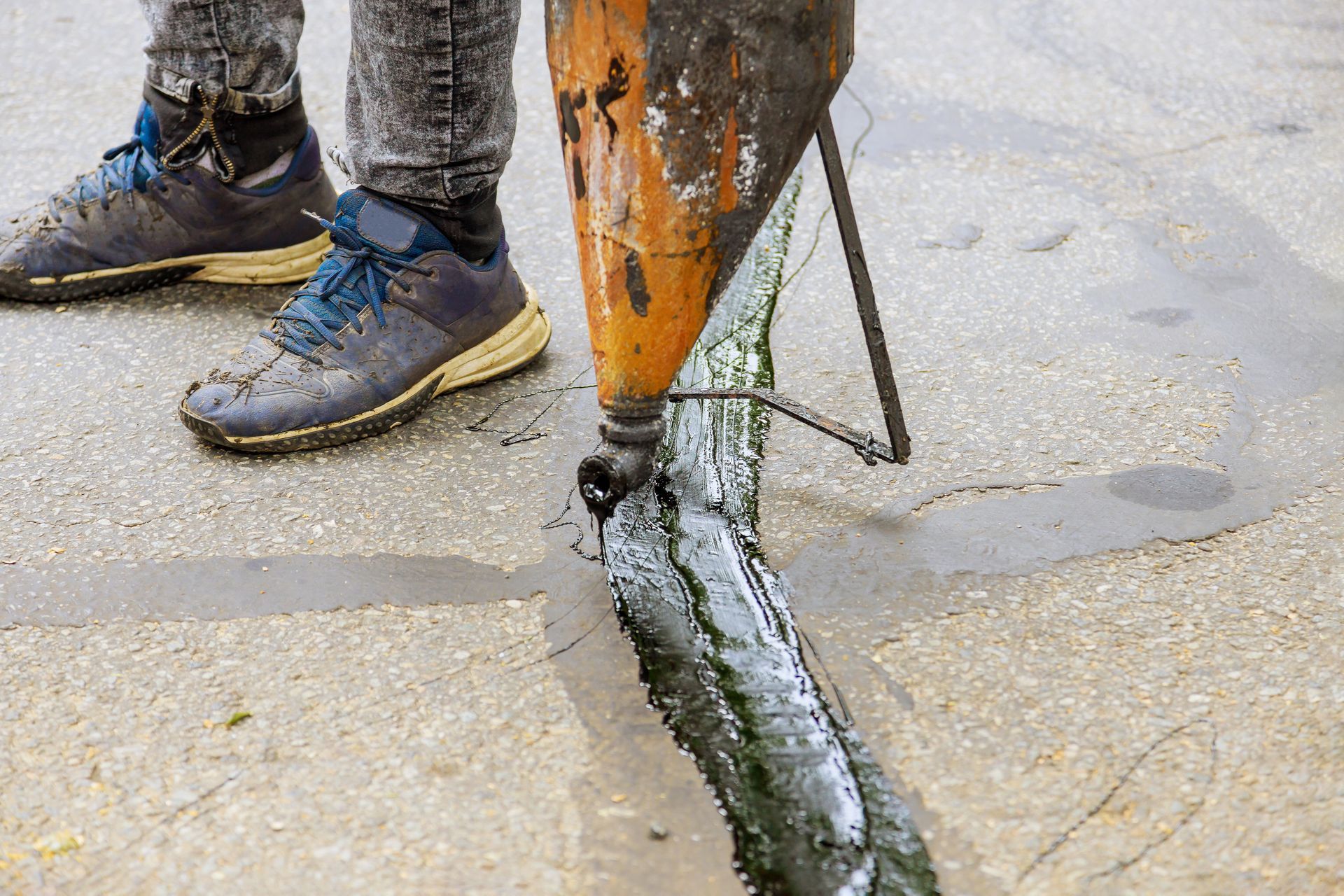 Worker’s boots beside a drill bit boring into wet concrete pavement