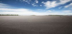 Empty gravel lot under a wide blue sky with distant trees on the horizon Empty gravel lot under a wide blue sky with distant trees on the horizon