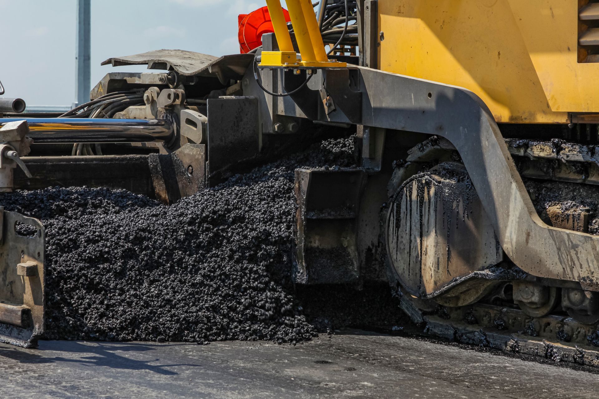 Road paver spreading fresh black asphalt on a street, with yellow machinery and a red warning flag. Road paver spreading fresh black asphalt on a street, with yellow machinery and a red warning flag.