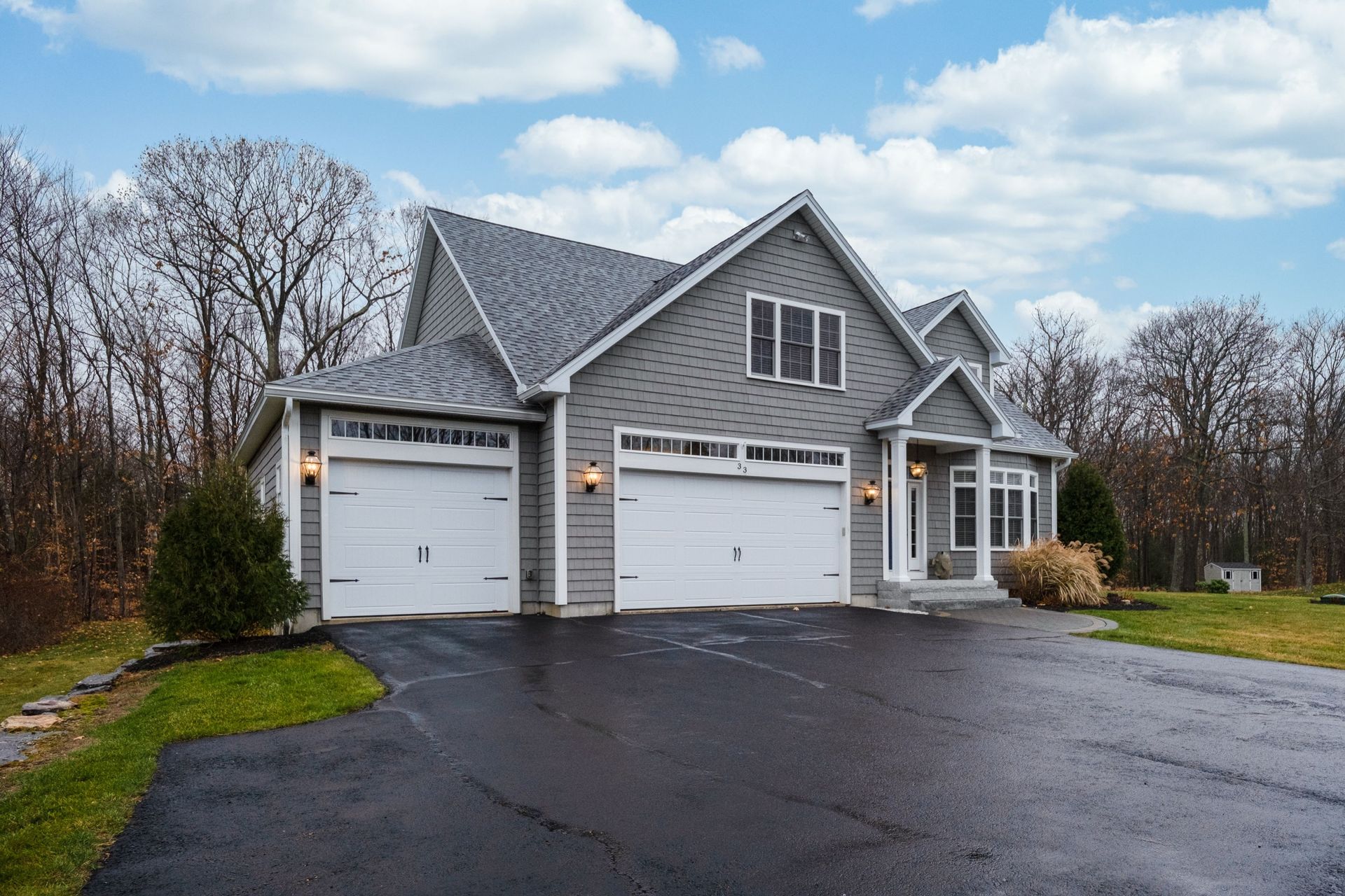 Gray house with two white garage doors and a wet driveway on an overcast day Gray house with two white garage doors and a wet driveway on an overcast day
