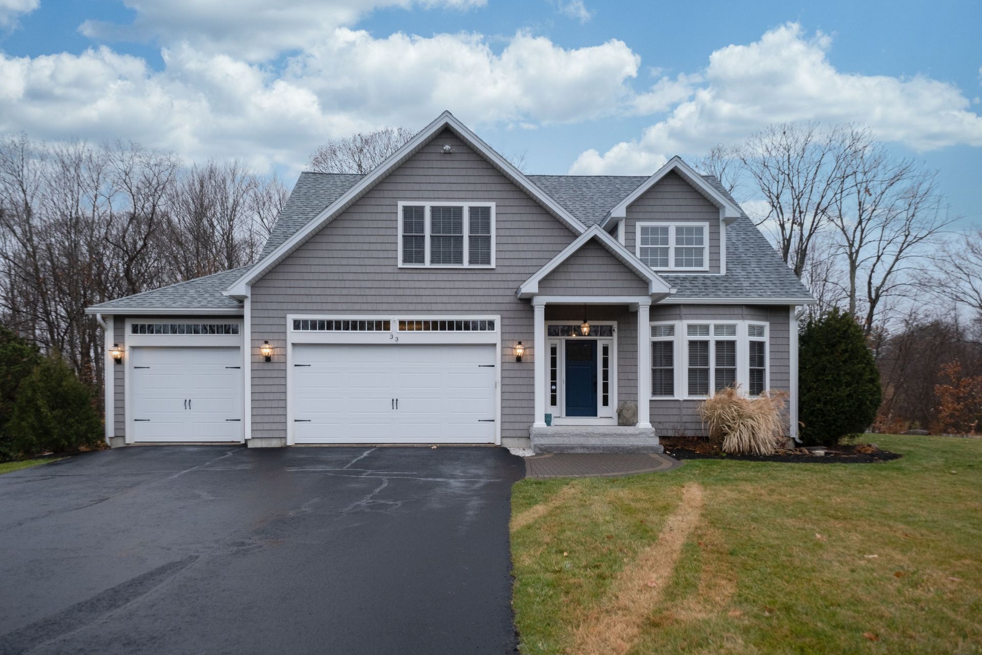 Gray suburban house with a two-car garage, front porch, and driveway on a cloudy day Gray suburban house with a two-car garage, front porch, and driveway on a cloudy day