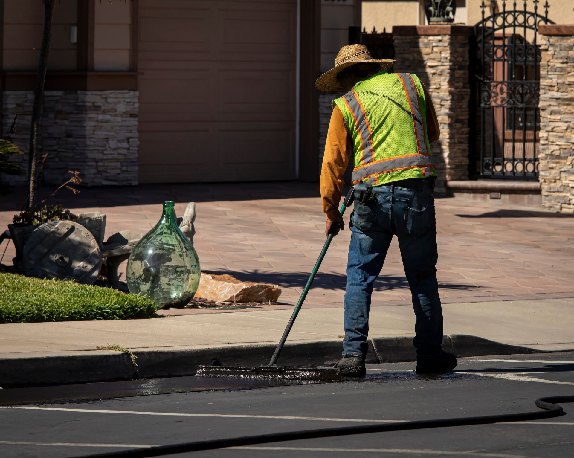 Worker in a reflective vest using a hose to wash a street curb beside a driveway. Worker in a reflective vest using a hose to wash a street curb beside a driveway.