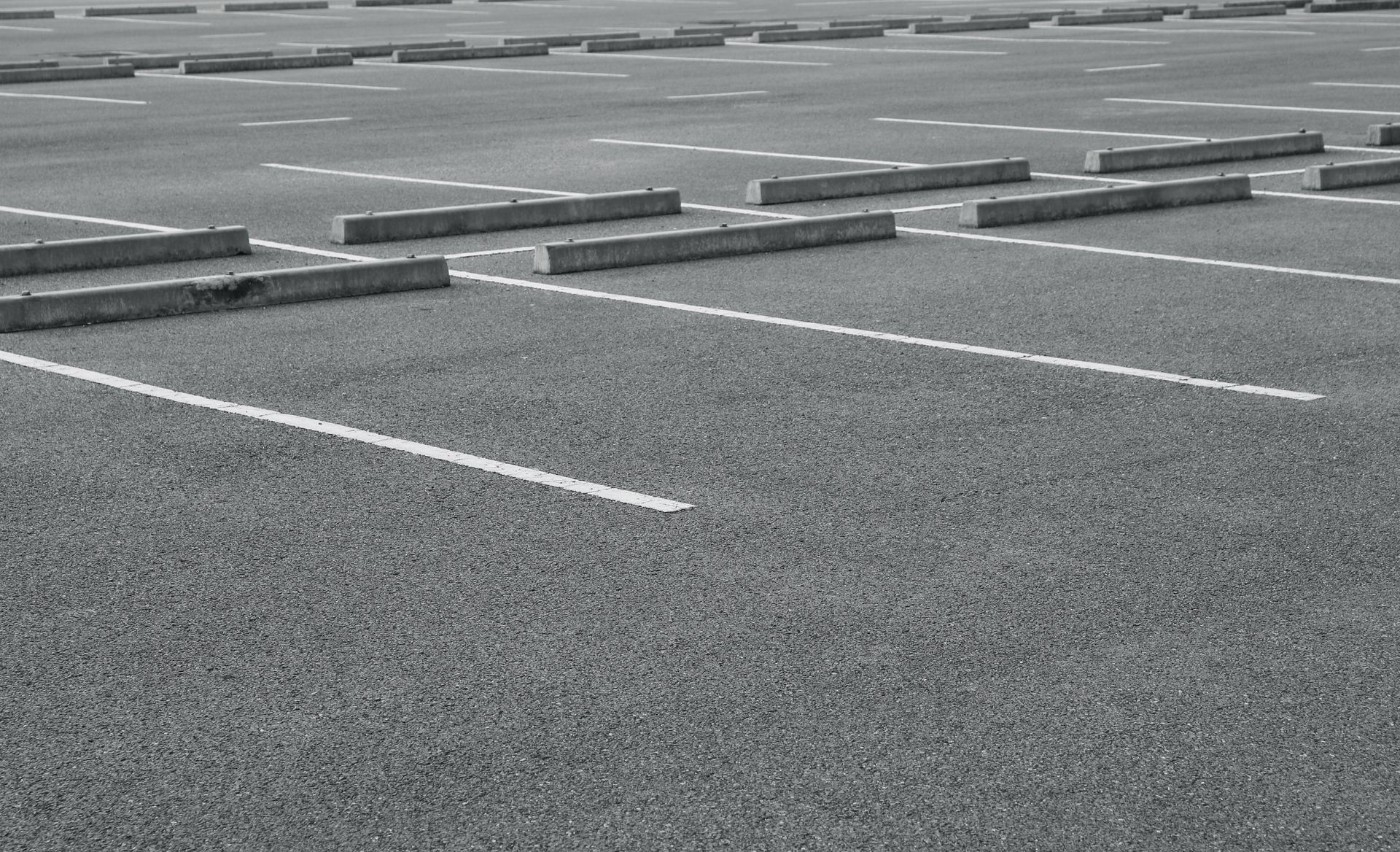 Empty parking lot with painted white lines and concrete wheel stops on a gray surface. Empty parking lot with painted white lines and concrete wheel stops on a gray surface.