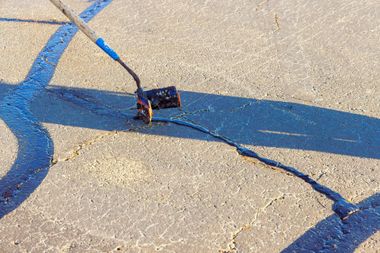 Small device with attached sticks on cracked concrete, casting a long shadow in sunlight