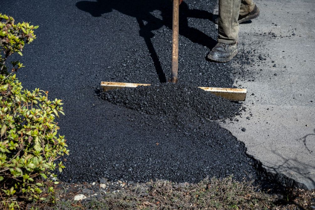Worker leveling fresh black asphalt with a rake on a roadside repair site Worker leveling fresh black asphalt with a rake on a roadside repair site