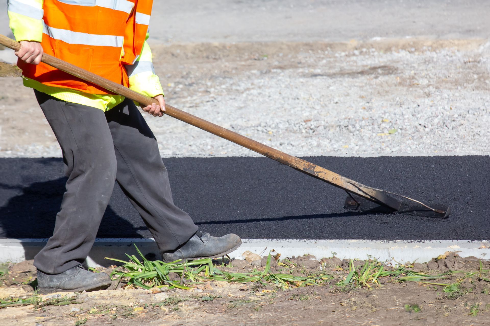 Road worker spreading asphalt with a shovel beside a fresh blacktop strip Road worker spreading asphalt with a shovel beside a fresh blacktop strip
