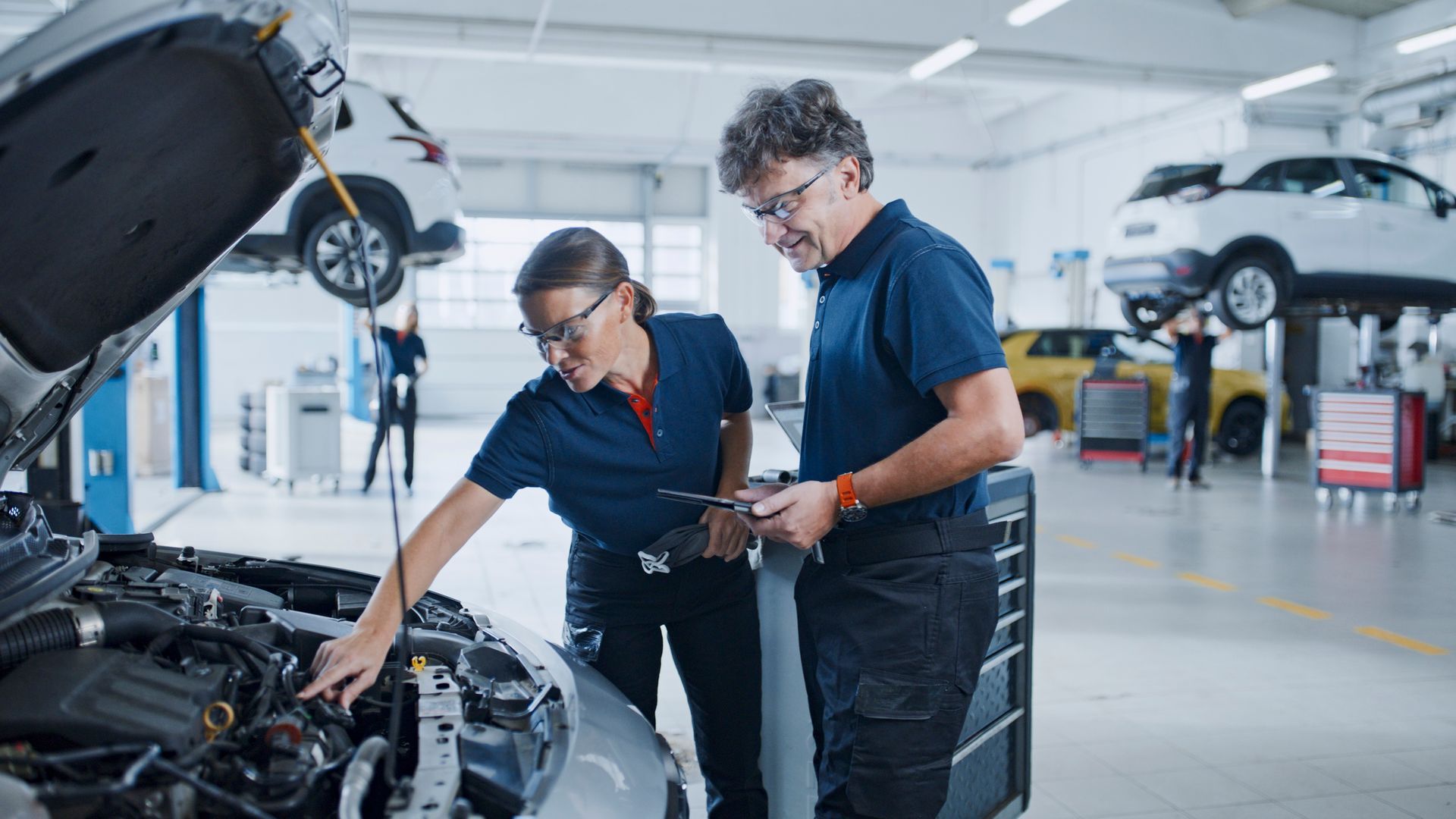 Two mechanics inspecting a car engine in a modern auto repair shop.