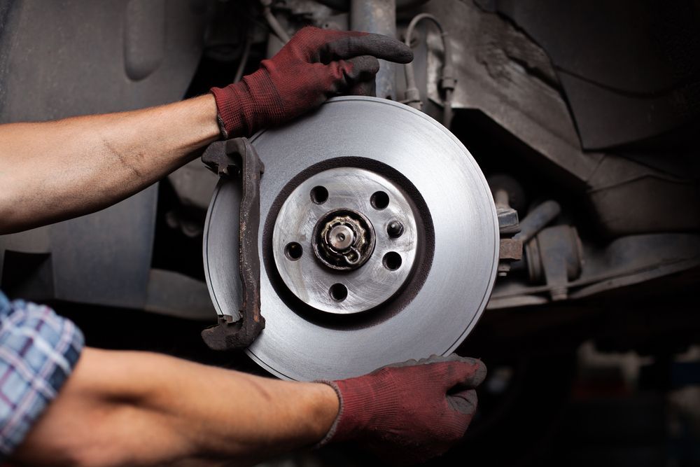 A Man is Fixing a Brake Disc on a Car — Marx Forster Tyres & Mechanical In Forster, NSW
