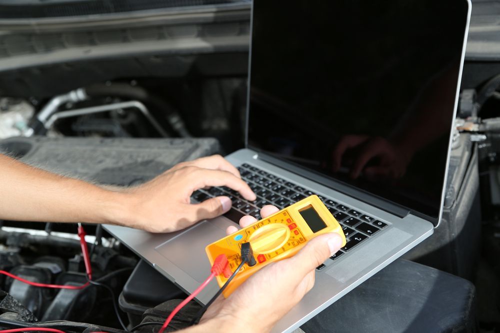 A Person is Working on a Laptop Computer While Holding a Multimetre — Marx Forster Tyres & Mechanical In Forster, NSW