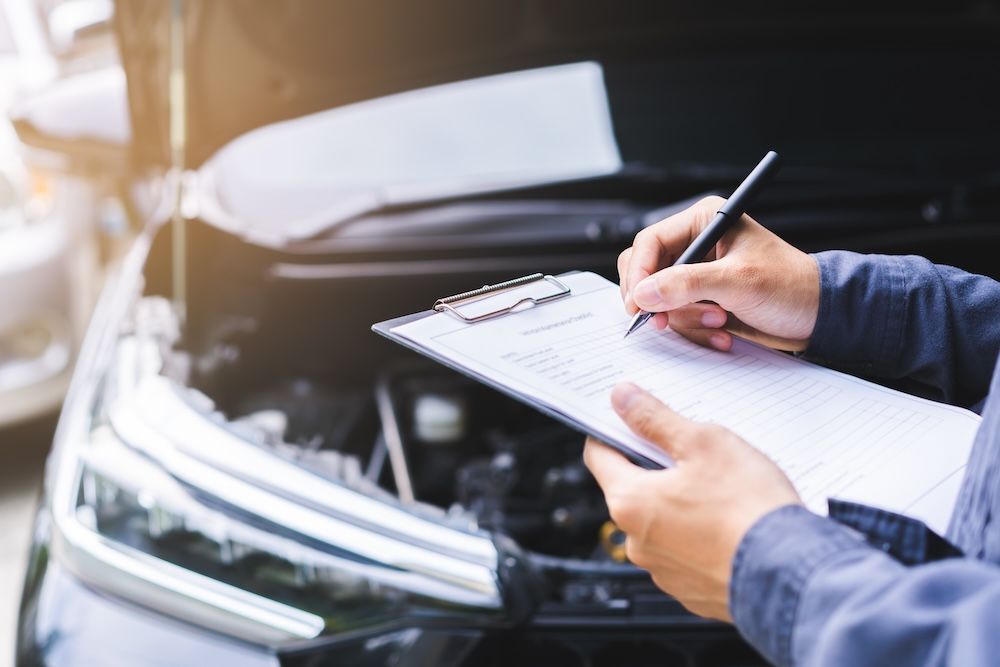A man is writing on a clipboard in front of a car — Marx Forster Tyres & Mechanical In Forster, NSW
