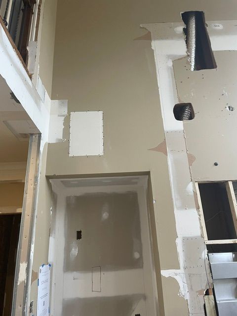 Construction in progress: walls with patched drywall and exposed framing, unfinished trim, tan paint, and electrical boxes.