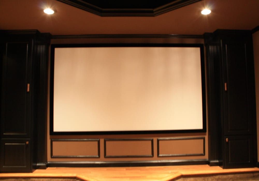 Home theater with large screen, built-in speakers and cabinets, and wood flooring.