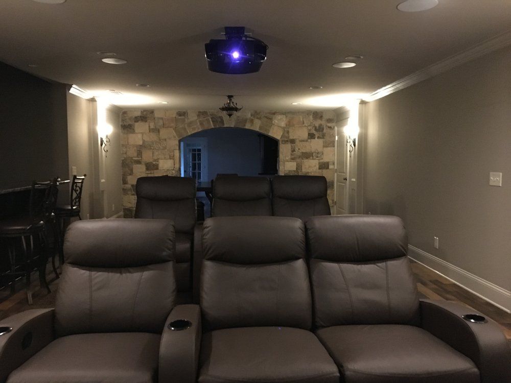 Home theater with brown leather recliners, projector, stone archway, recessed lighting.