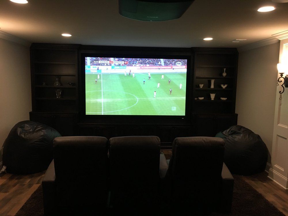 Home theater with a large screen showing a soccer game. Dark seating and bean bags.