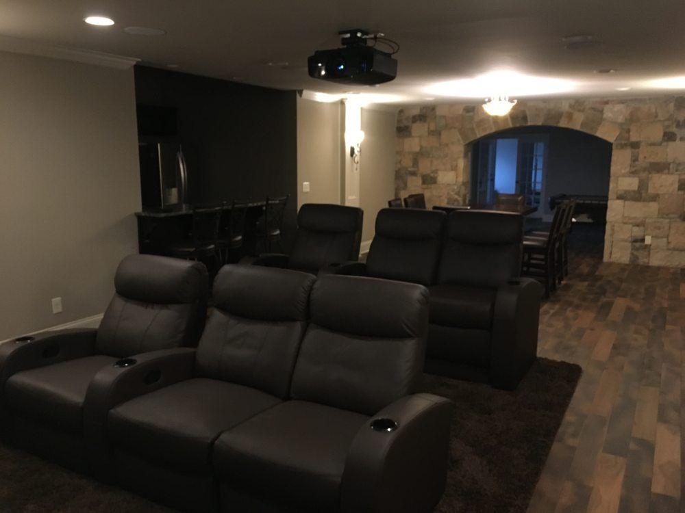 Home theater with black leather seating, a projector, and a stone archway.