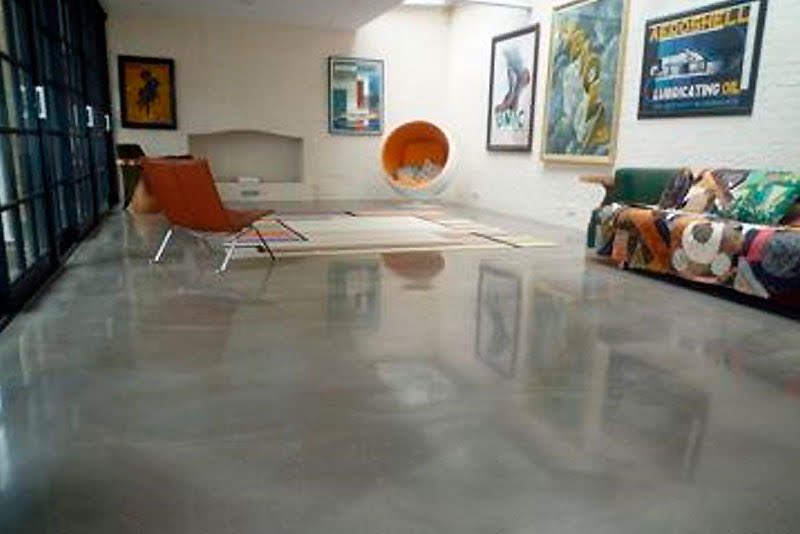 Modern living room with polished concrete floor, orange chair, colorful couch, and wall art