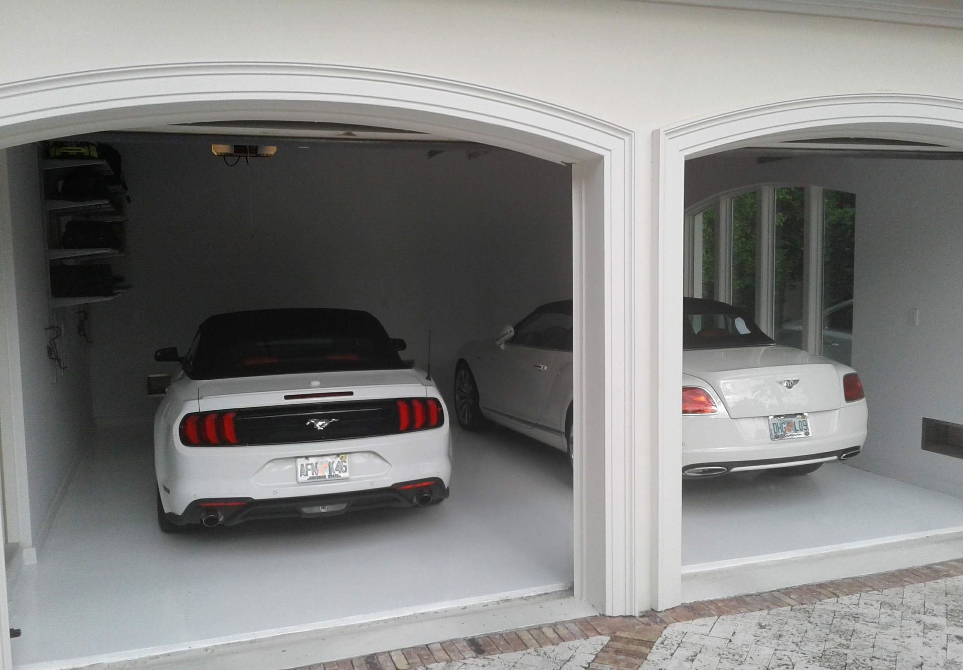 Two cars parked in a two-car garage, including a white sports car and a white sedan.