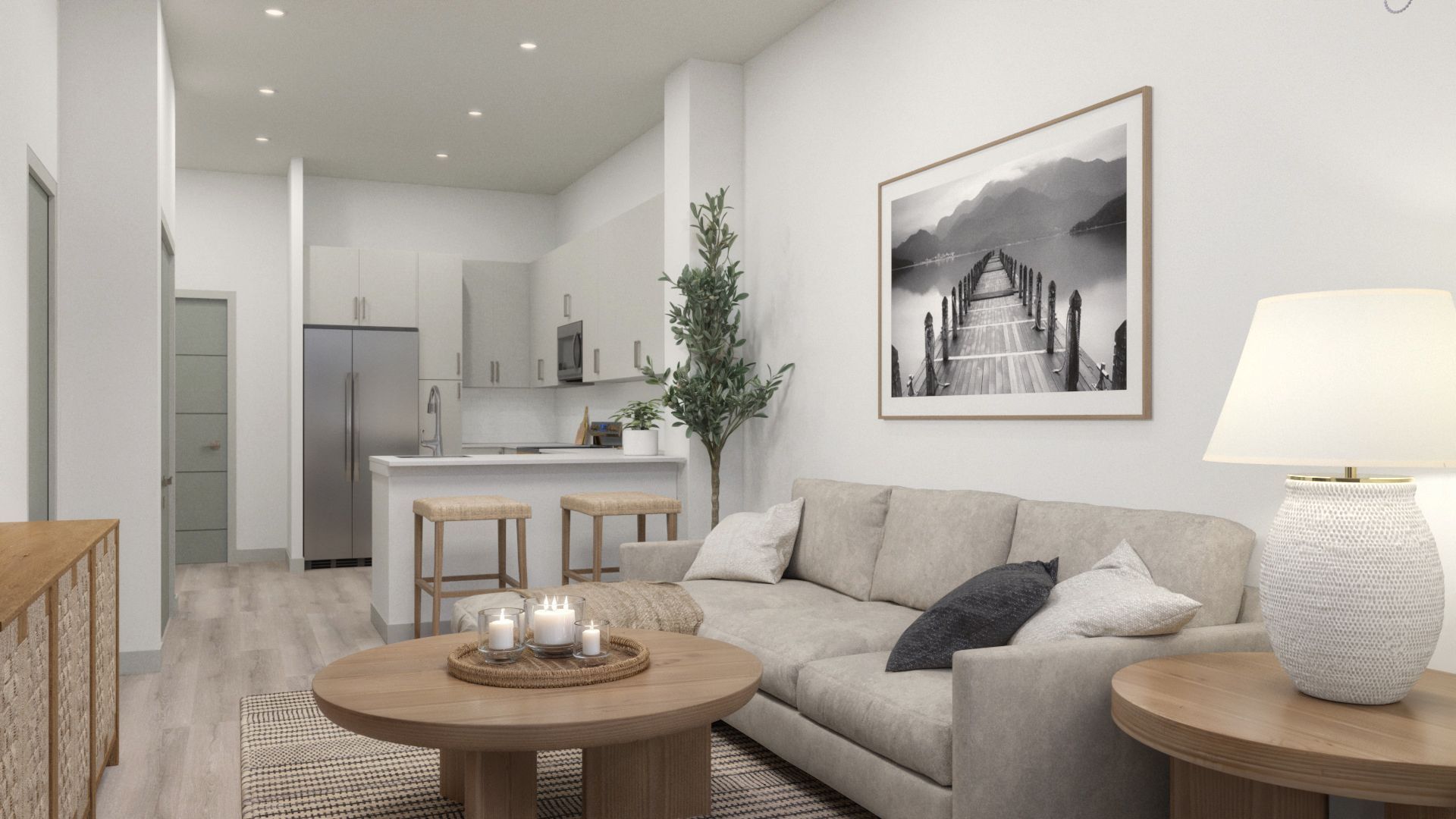 Modern open-plan living room with beige sofa, round coffee table, framed art, and a kitchen in the background