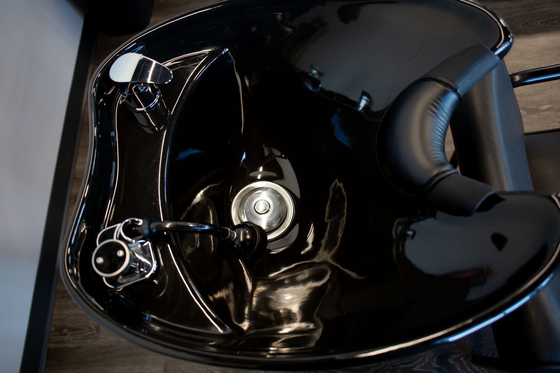 A glossy black salon shampoo bowl with chrome fixtures and a padded neck rest, viewed from above.