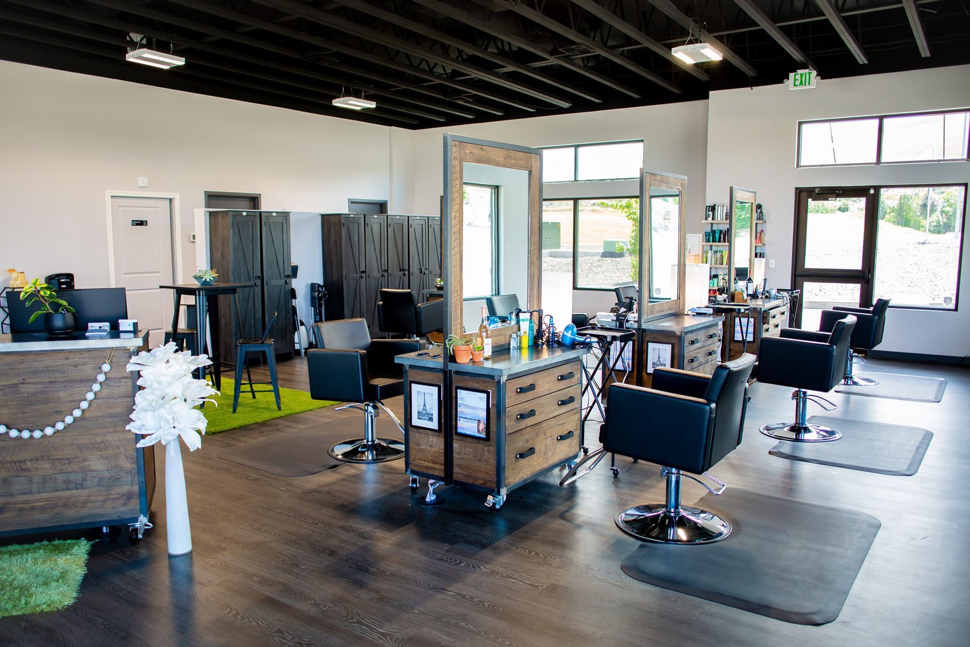 A bright hair salon interior featuring several styling stations with chairs, mirrors, and wooden drawers on a dark floor.