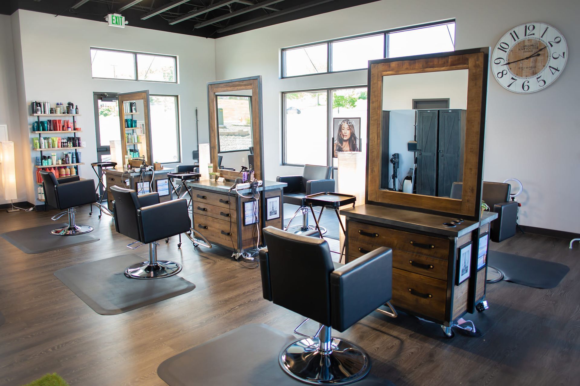Modern hair salon with three styling stations featuring dark wood cabinets, mirrors, and black chairs on a wood floor.