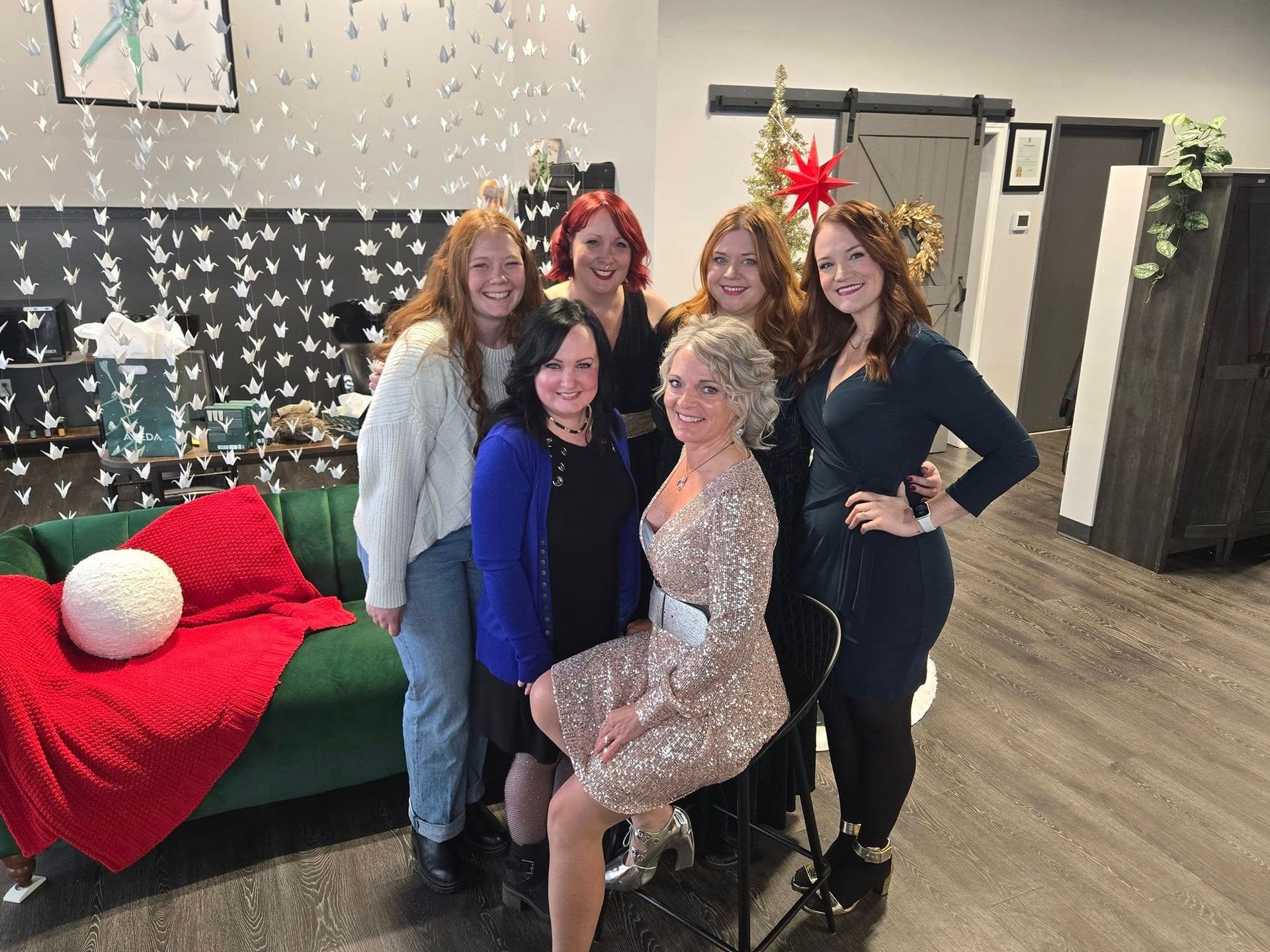Six people pose together for a photo in front of a green couch, a decorated tree, and a wall of hanging paper birds.