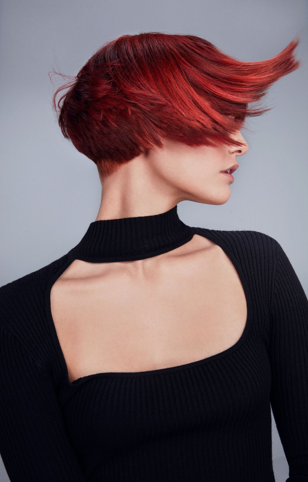 A person with a short, vibrant red asymmetrical hairstyle against a plain light gray background.