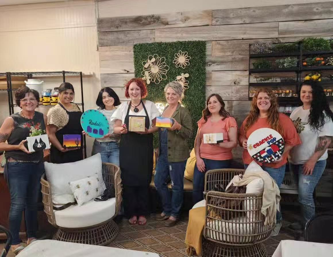A group of eight people pose in a craft studio, smiling and holding their handmade painted projects.