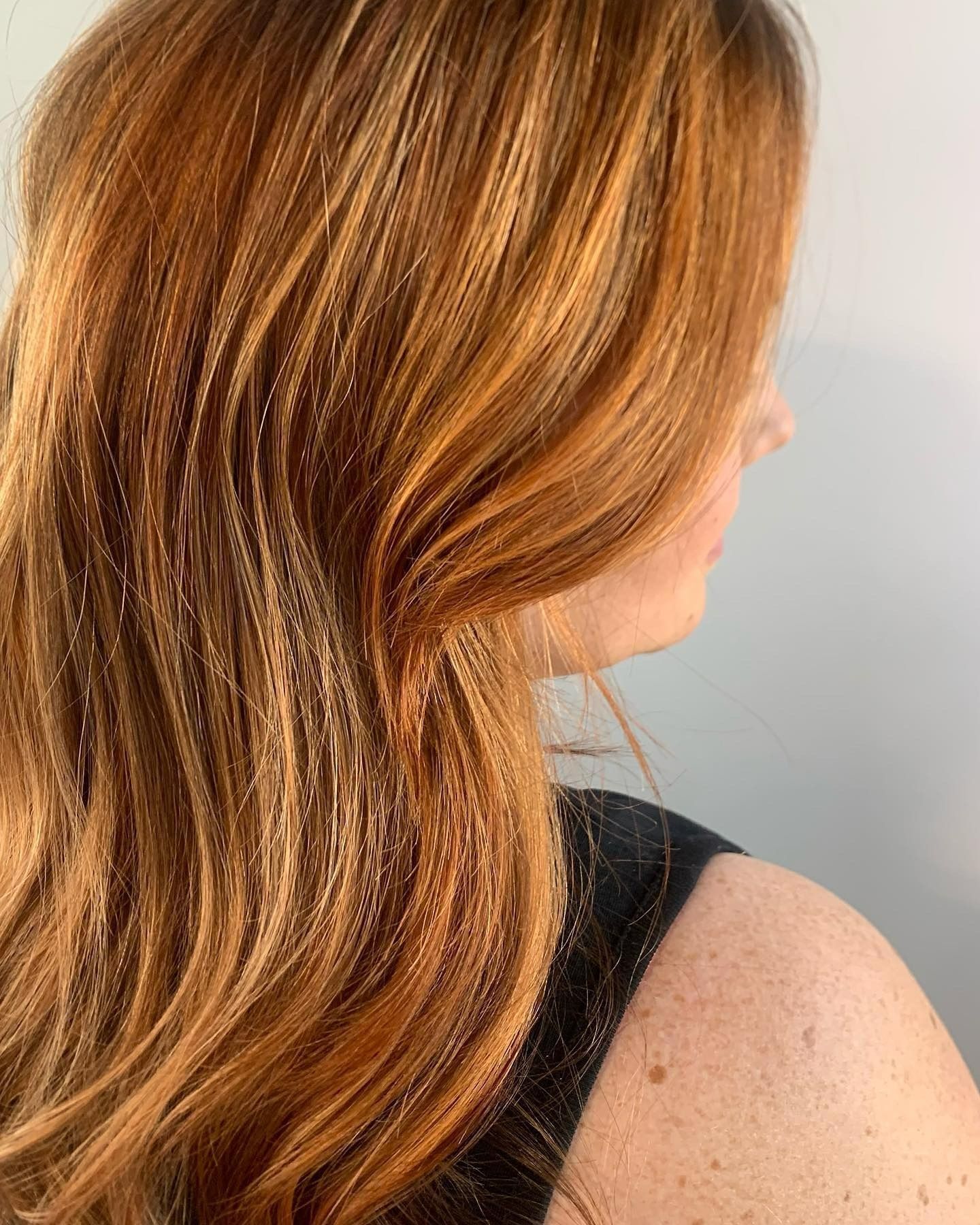 A person with wavy, copper-toned hair styled with subtle blonde highlights, shown from the back and side.