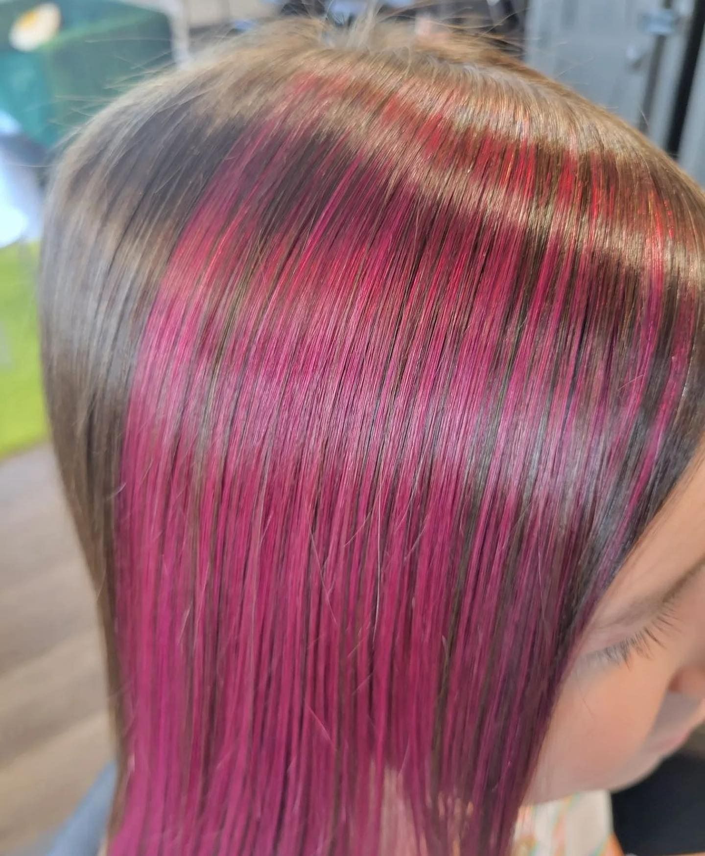 A close-up of brown hair featuring bright pink, vertically placed highlights.