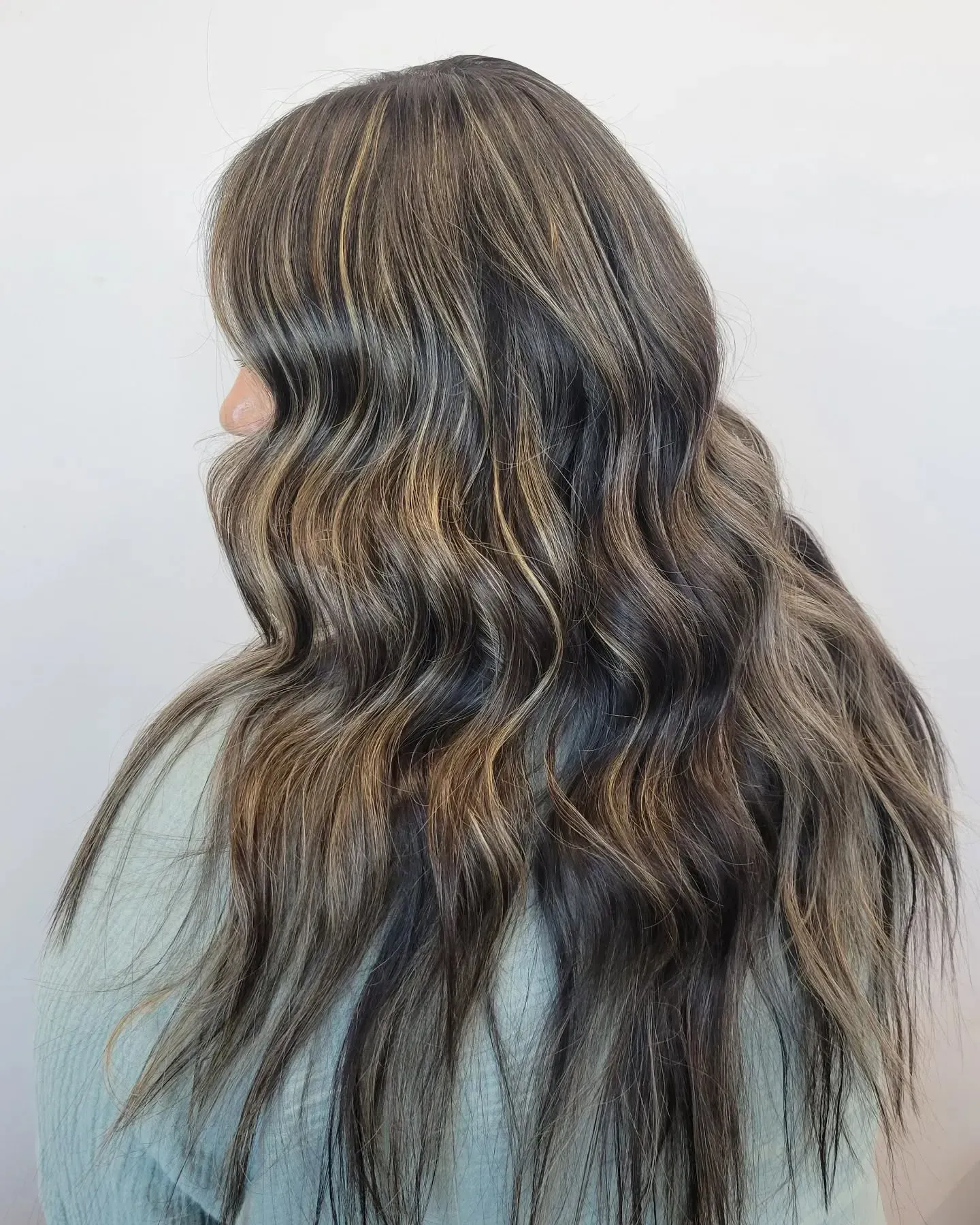 Long, wavy hair with brunette base and dimensional blonde highlights against a plain white background.