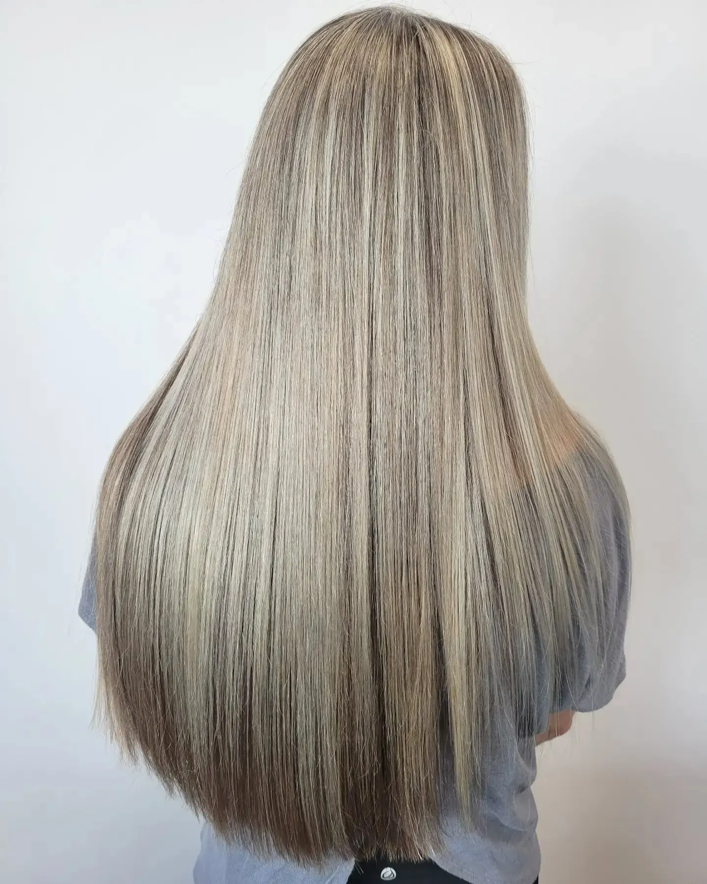 A person with long, straight, ash-blonde hair with a crimped texture seen from behind against a plain white background.