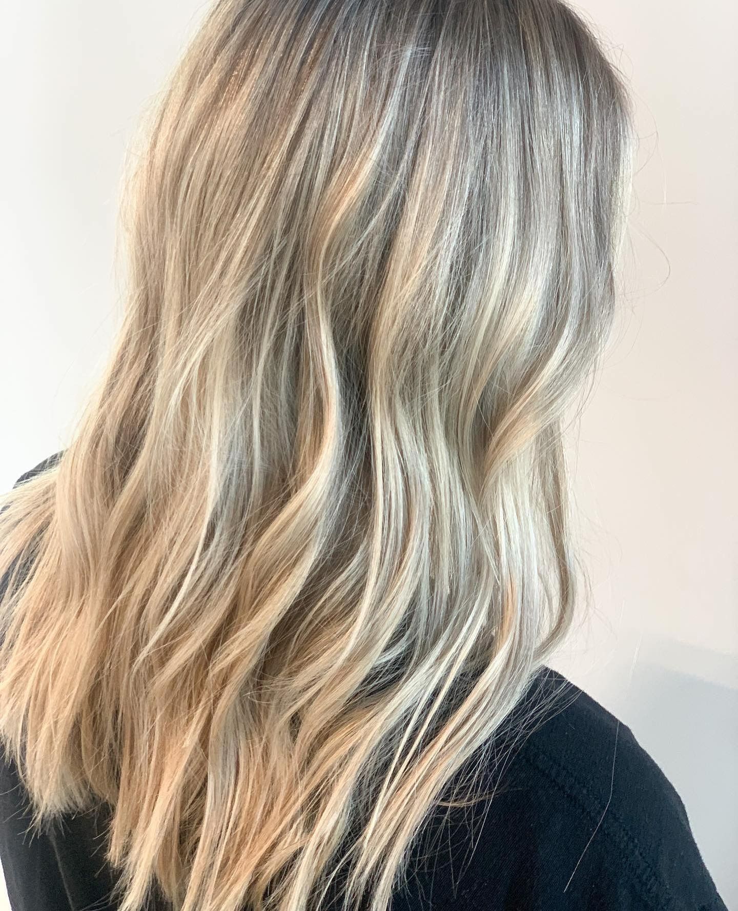 Wavy hair with a balayage coloring technique blending dark roots into blonde and cool-toned highlights.