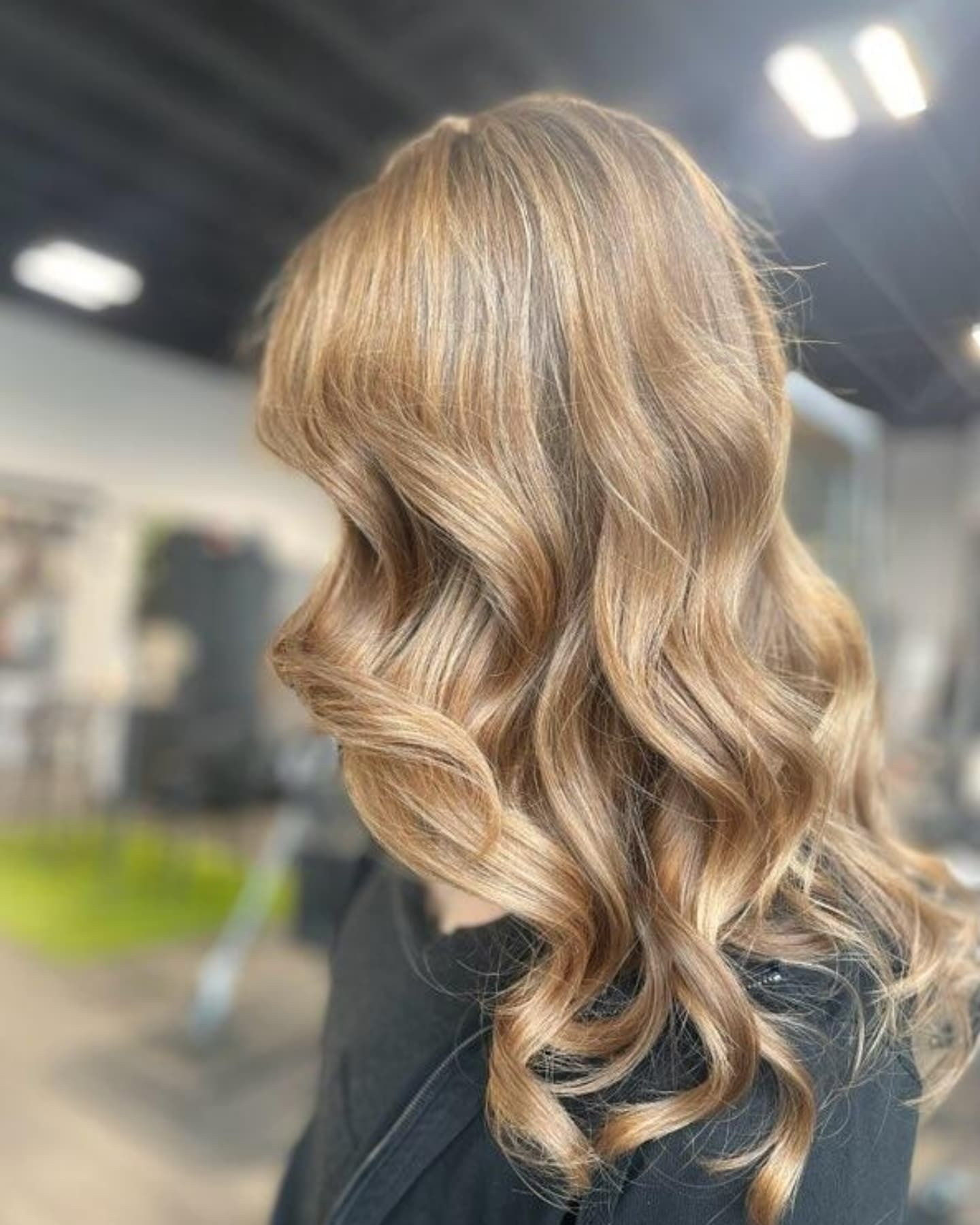 Shoulder-length, wavy light brown hair styled in soft curls against a blurred indoor salon background.