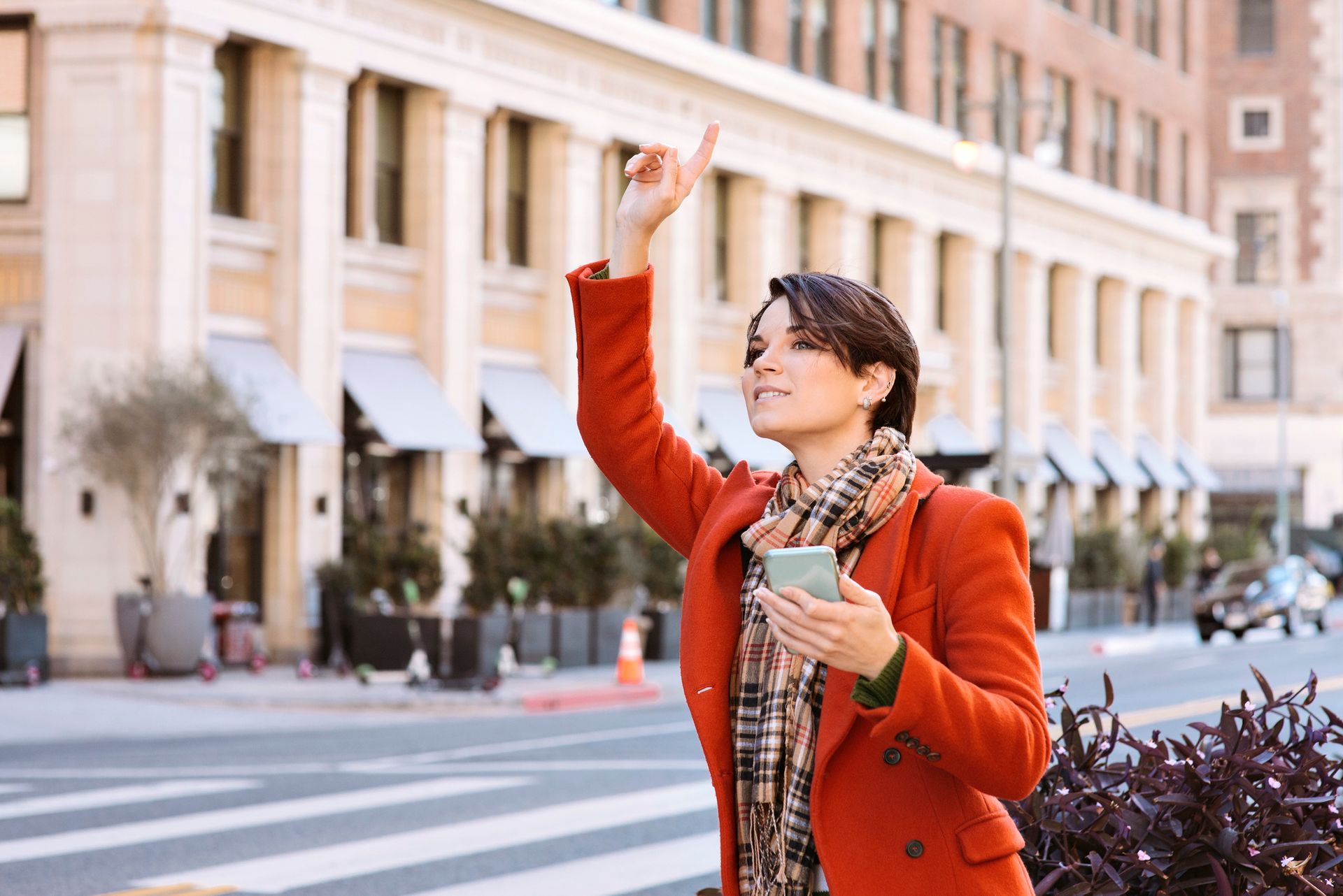 Woman in orange coat hailing a cab on a city street, holding phone, looking up. Woman in orange coat hailing a cab on a city street, holding phone, looking up.