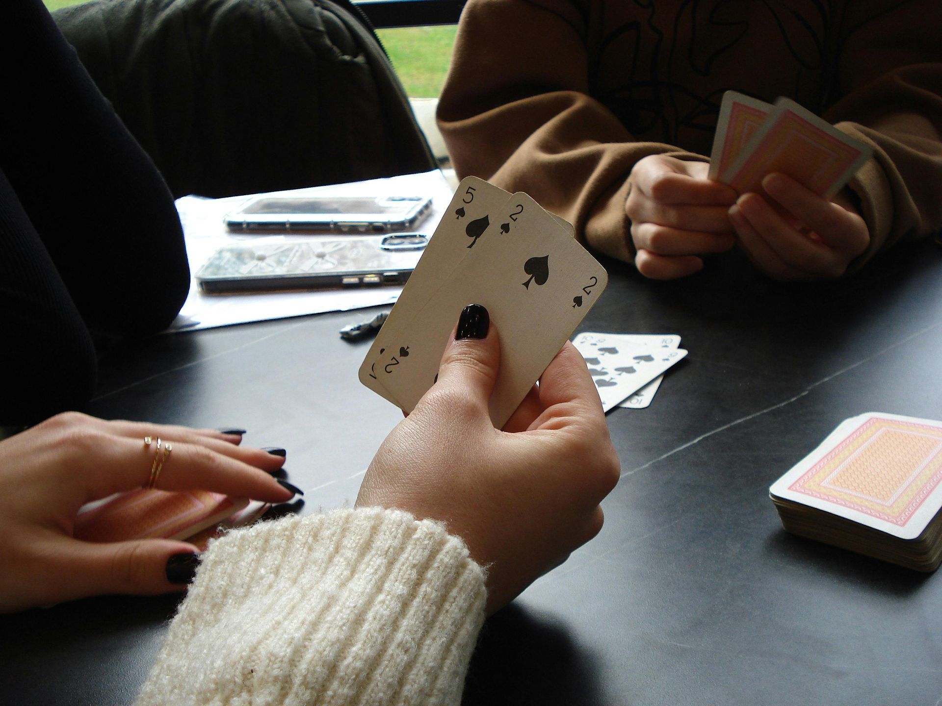 A person spreads tarot cards on a red tablecloth with a glowing crystal ball nearby in a dimly lit room.