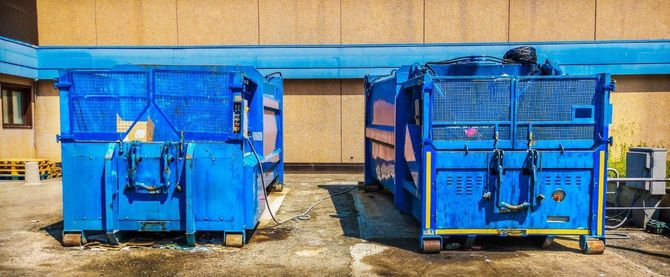 Two blue industrial dumpsters in a warehouse loading area