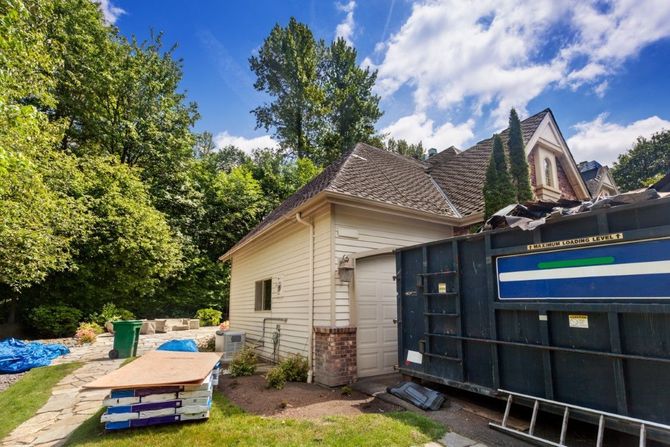 Backyard with a cream shed, blue dumpster, stacked wood, and trees under a partly cloudy sky