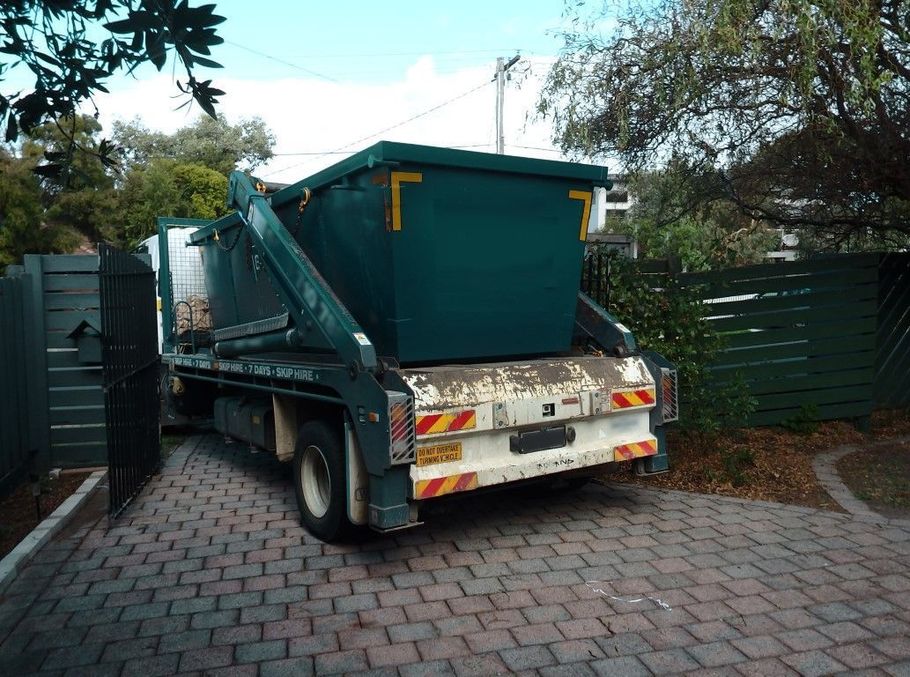 Garbage truck parked in a driveway, carrying a large green dumpster.