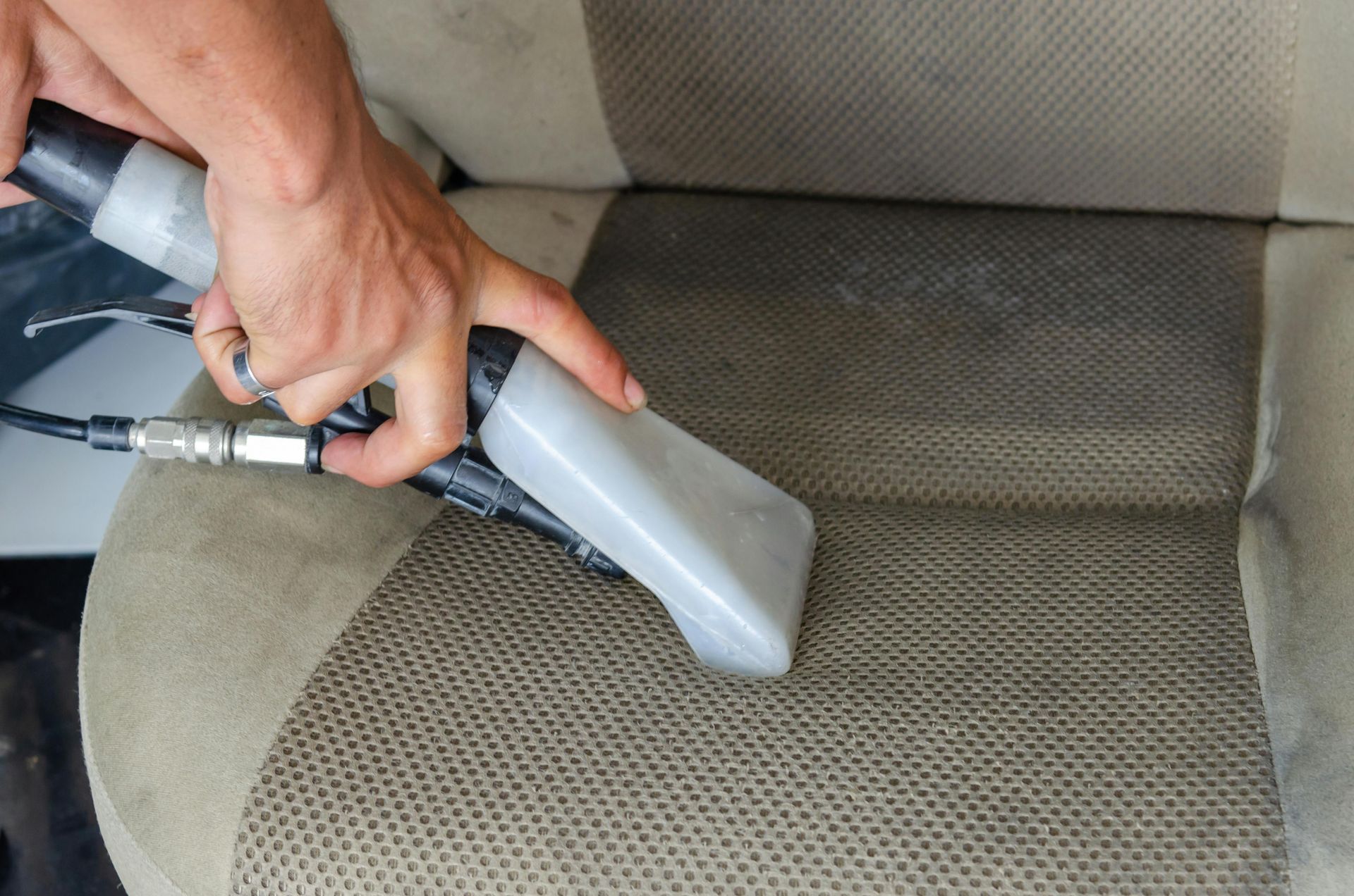 Professional car seat steam cleaning with upholstery extractor tool.