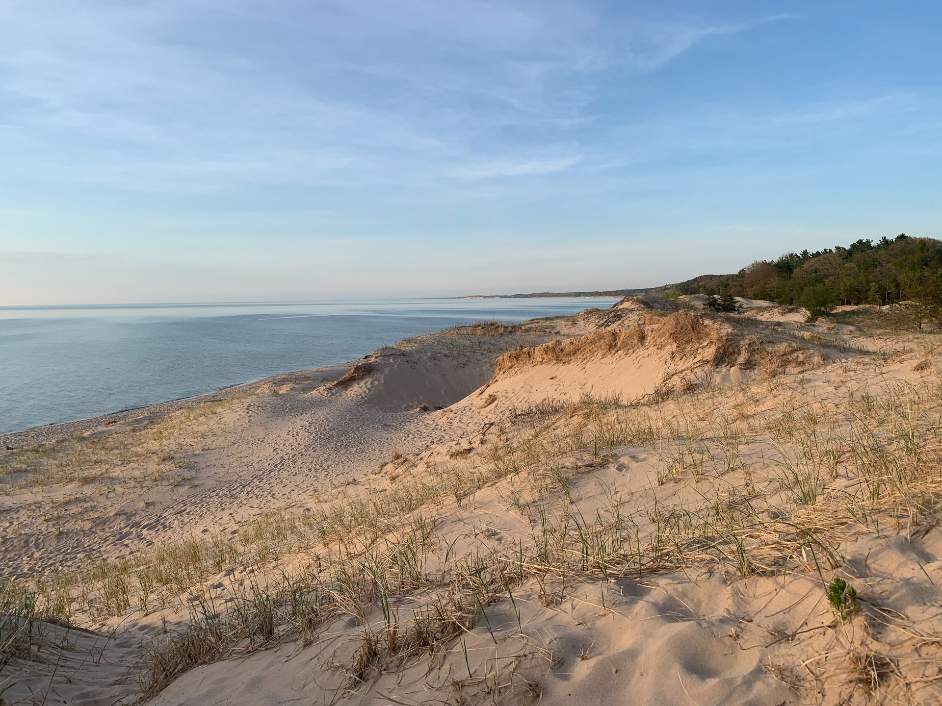 Sandy dune and calm ocean shoreline under a blue sky at sunset