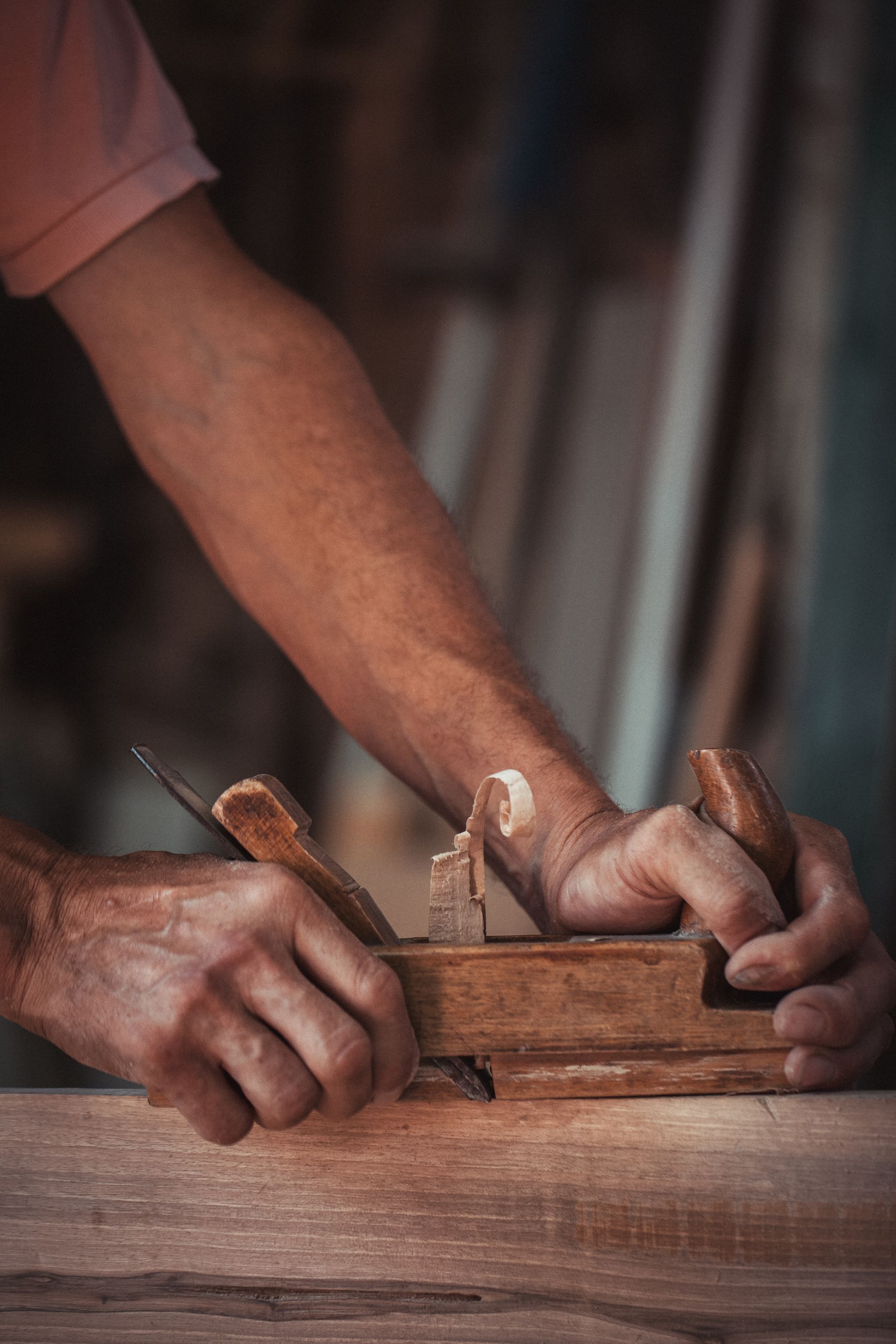 Hands using a woodworking hand plane on a wooden board in a workshop